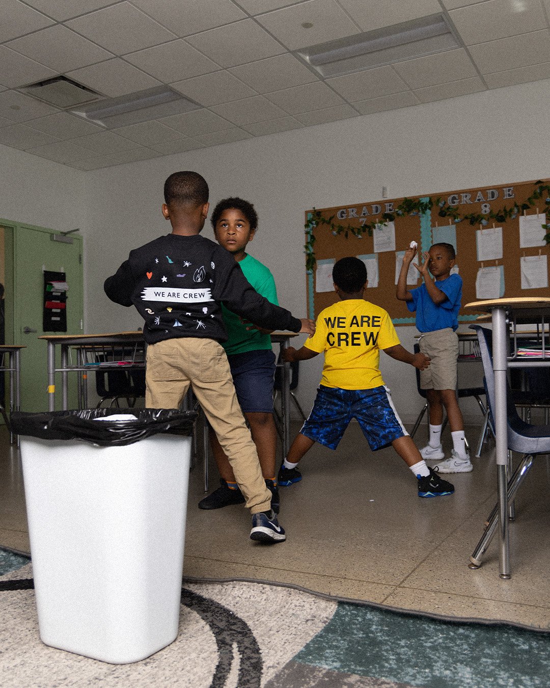 Students playing in a classroom, backs showing the We Are Crew prints