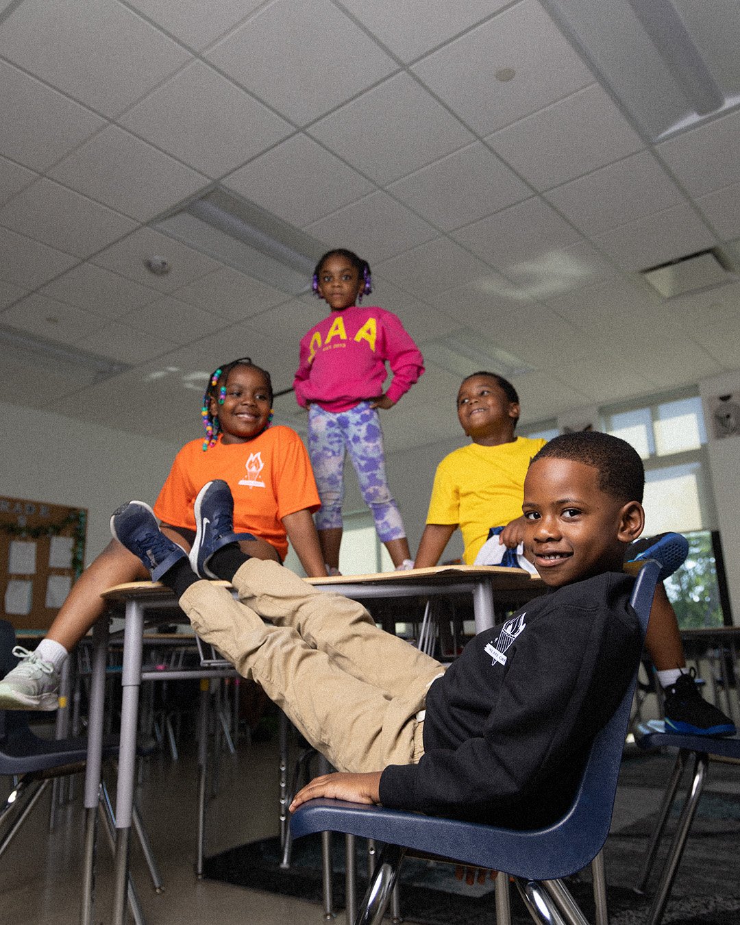 Students on and around classroom desks in We Are Crew tees and a pink D.A.A. crewneck