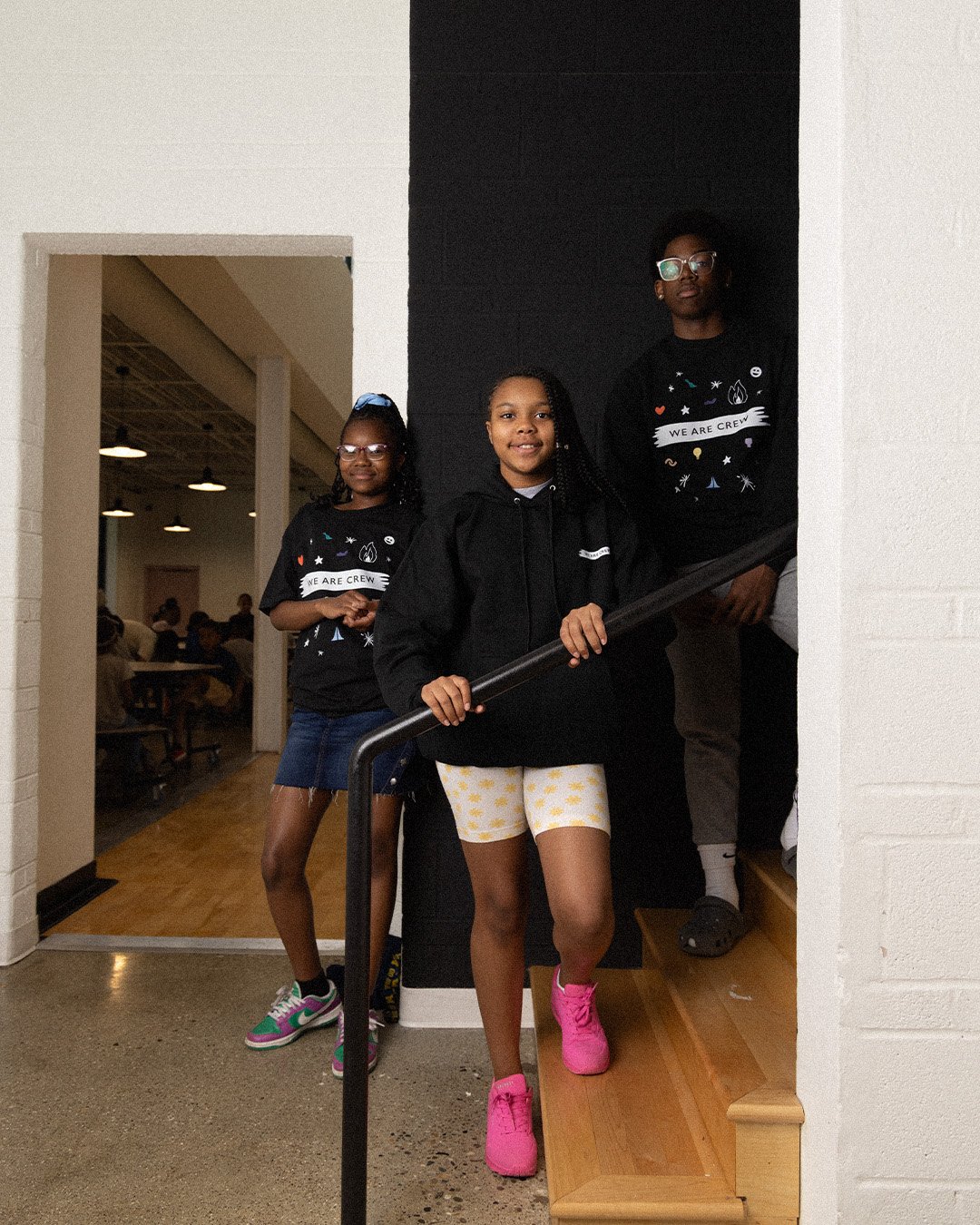 Three students on the stairs in the black We Are Crew tee, hoodie and crewneck
