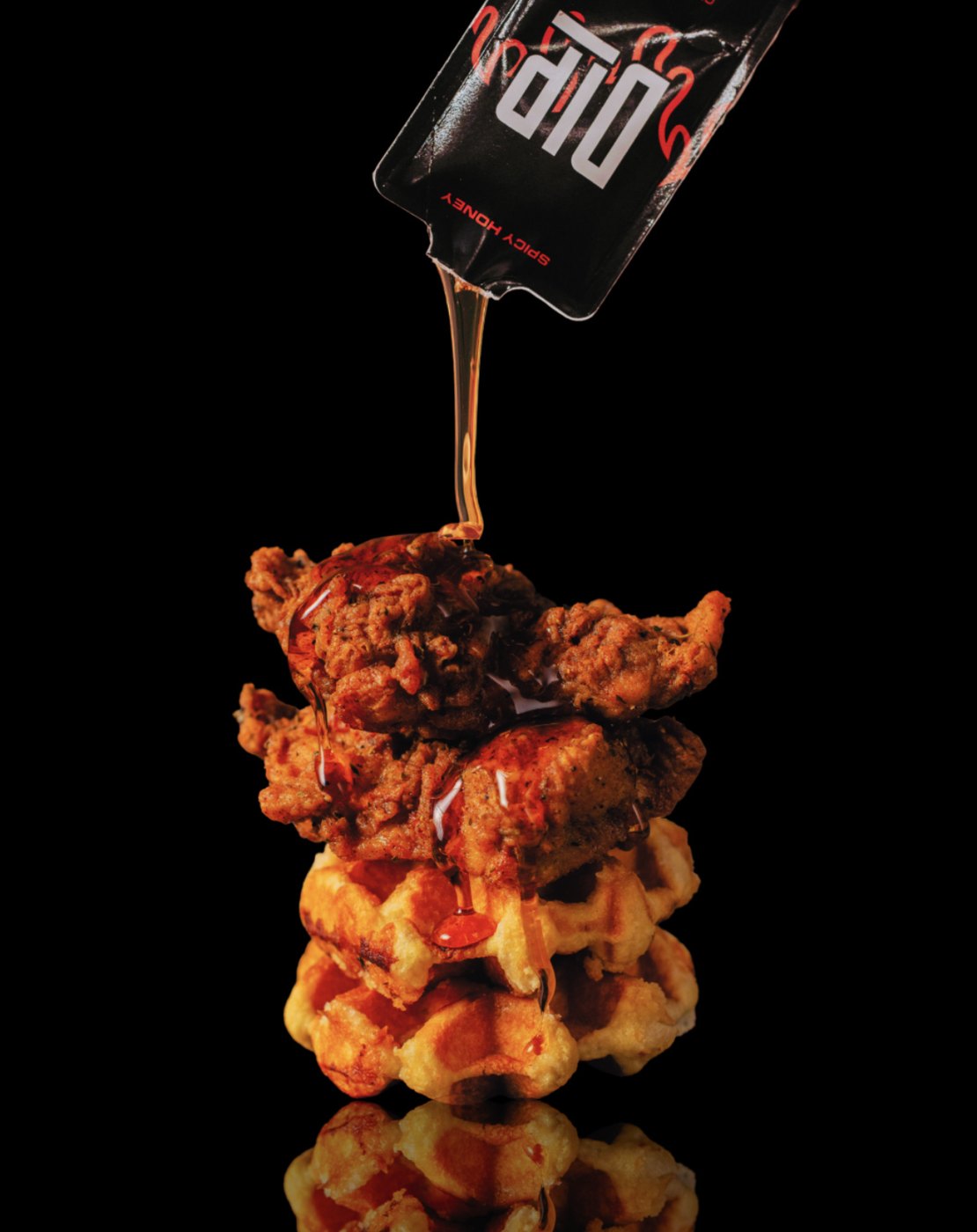 DIP spicy honey poured from a packet onto chicken and waffles